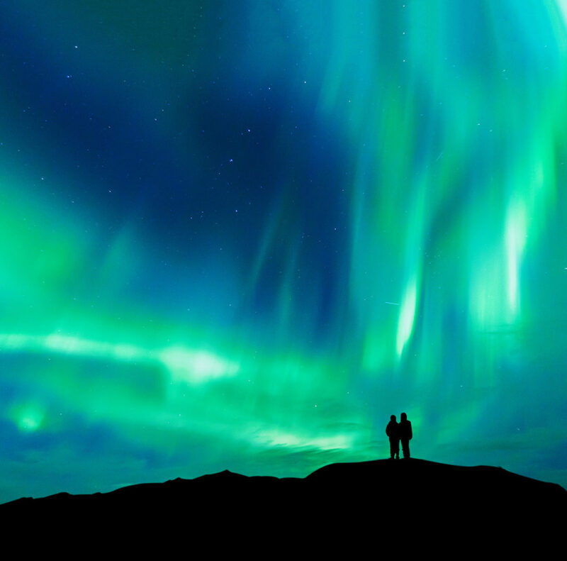 Silhouette of a couple watching the bright green northern lights in a starry night sky during luxury trips for two.
