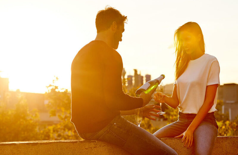 Man pouring champagne for a woman at sunset on a rooftop during luxury Honeymoons.