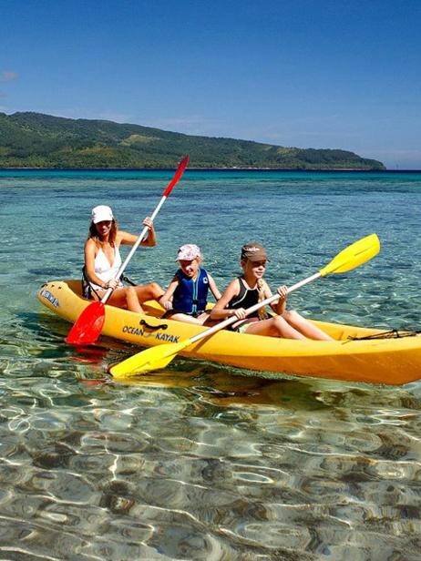 People in a yellow kayak on crystal clear ocean water with hills in the background on luxury Family vacations.