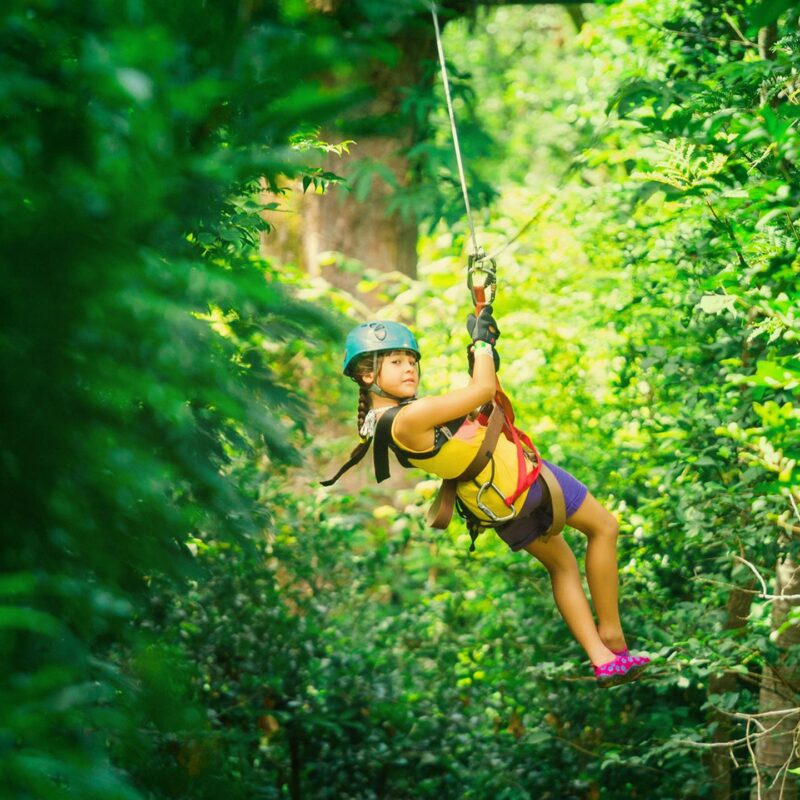 A young girl glides through the dense green rainforest canopy on luxury Latin America family vacations.