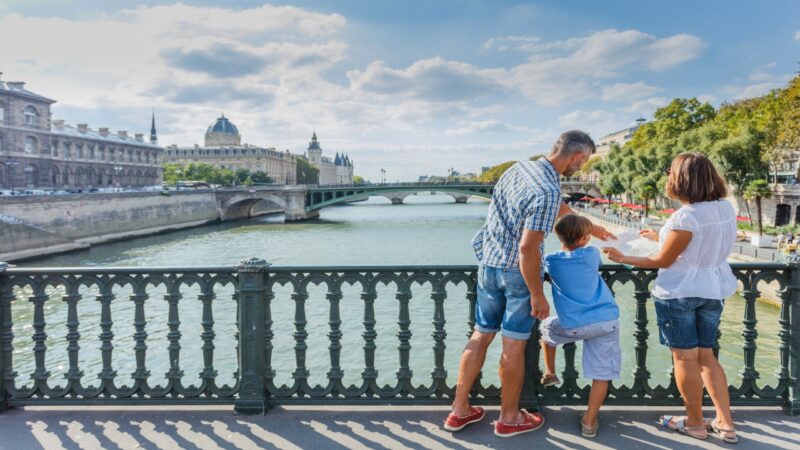 A family of three looking at a map on a bridge over the river in central Paris on a sun-soaked day