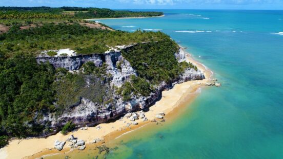 The turquoise water calmly lapping the golden sands that surround the tree-lined cliff.