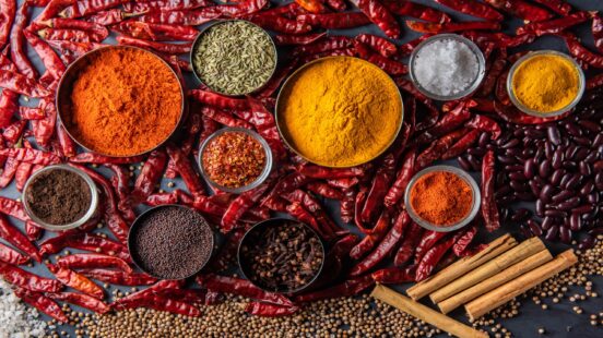 Overhead view of colorful spice powders and whole spices in small bowls on a bed of dried chilis.