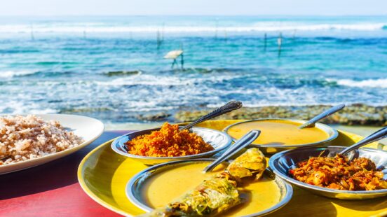 A traditional meal of rice and various curries served in bowls on a table overlooking the ocean.