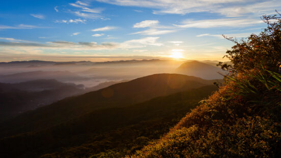 Golden sun rising over silhouetted mountain peaks covered in a thick layer of morning mist.