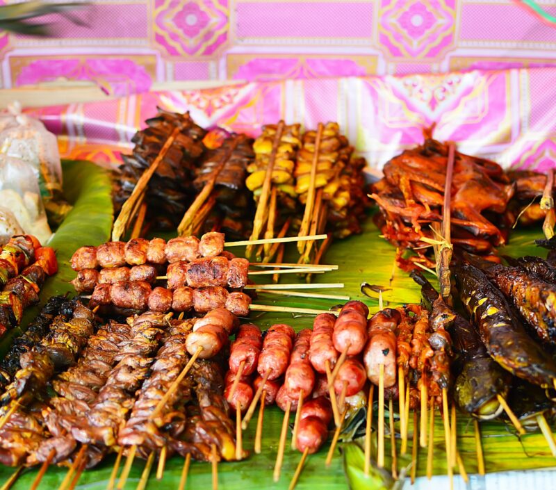 Assorted grilled meat and fish skewers served on green banana leaves, a taste of luxury Laos holidays.
