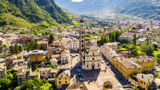 High-angle view of a town with a prominent stone church tower and surrounding buildings in a green valley.