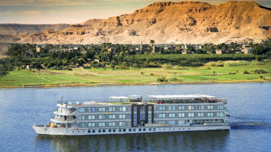 The Historia cruise ship sailing on the Nile River with green fields and arid mountains in the background.