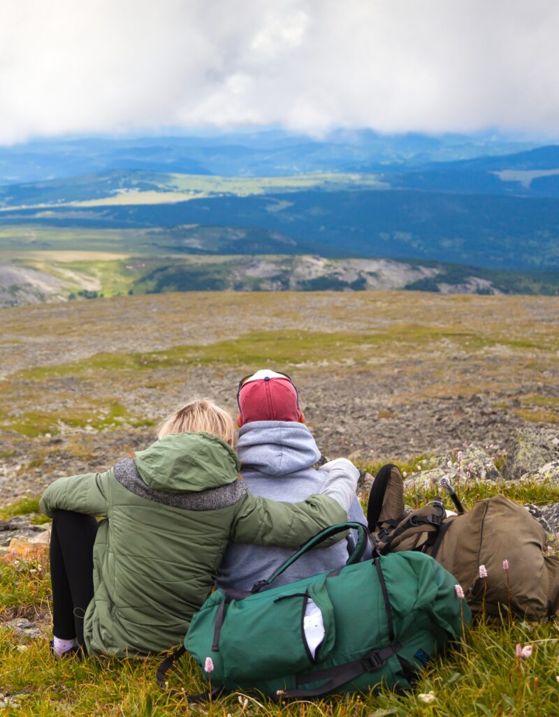 Travel Lifestyle and survival concept rear view.Hiking lovers woman and man with backpack is sitting on the top of the mounting and looking at a beautiful landscape.