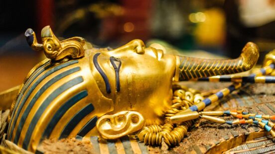 Close-up side view of a gold Egyptian pharaoh mask with blue stripes and a decorative vulture and cobra.