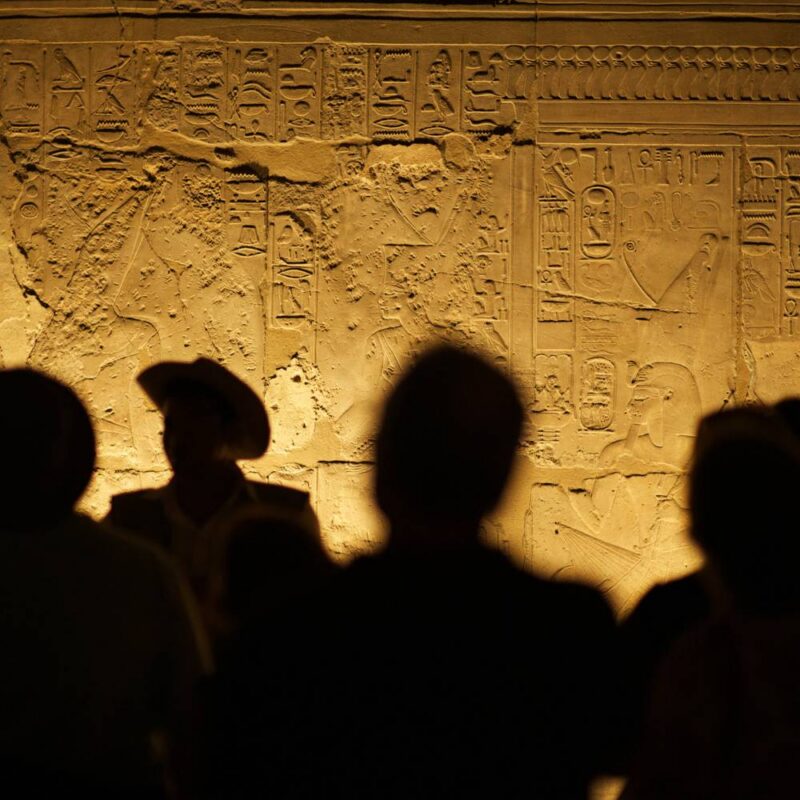 Luxury Egypt Tours - silhouettes of people looking at ancient hieroglyphs on a lit wall