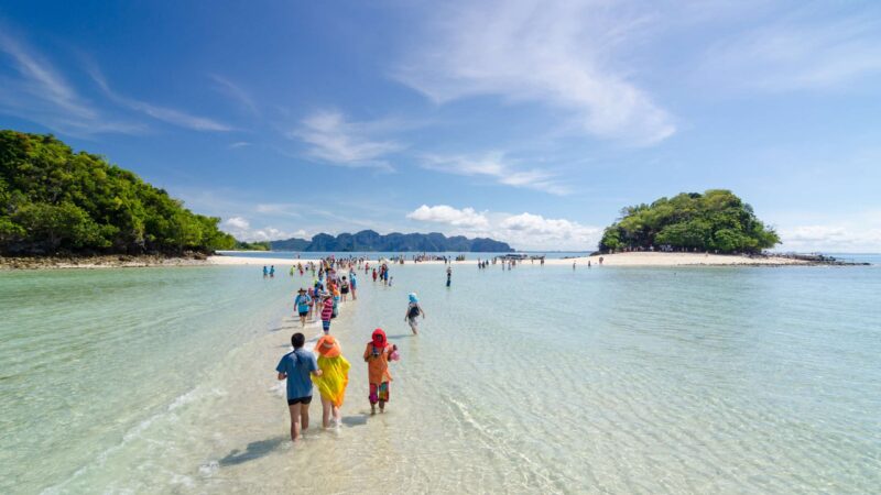 People walking along a tropical sandbar in clear water during luxury asian family trips.