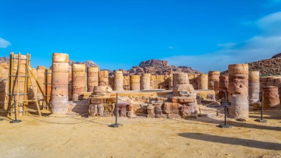 Several weathered stone columns and archaeological ruins stand under a blue sky in the ancient city of Petra.