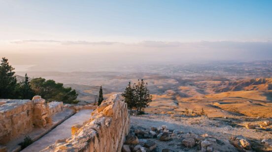 A panoramic view of a hazy desert valley seen from an ancient stone wall viewpoint.
