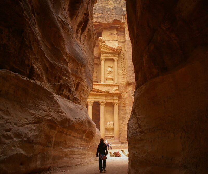 A traveller walks through the narrow Siq, catching their first glimpse of Petra's Treasury in Jordan.