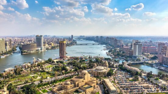High angle view of the Nile River winding through a dense city with bridges, parks, and high-rise buildings.