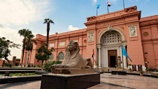 Front view of the Egyptian Museum building in Cairo with a large sphinx statue and palm trees.