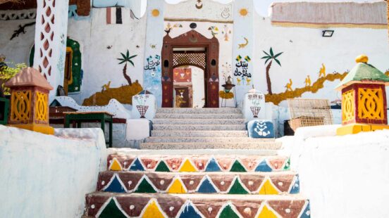 Vibrant stairs with colorful patterns leading to a white house adorned with palm tree and camel paintings.