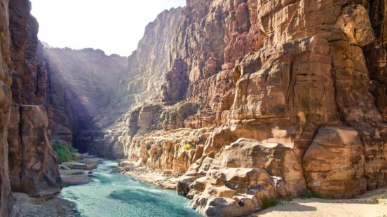 A bright blue river winds through a deep canyon with high, rugged rock walls.