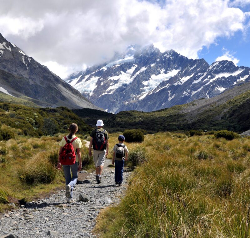 Family walking down a rocky trail with large snowy mountains in the distance