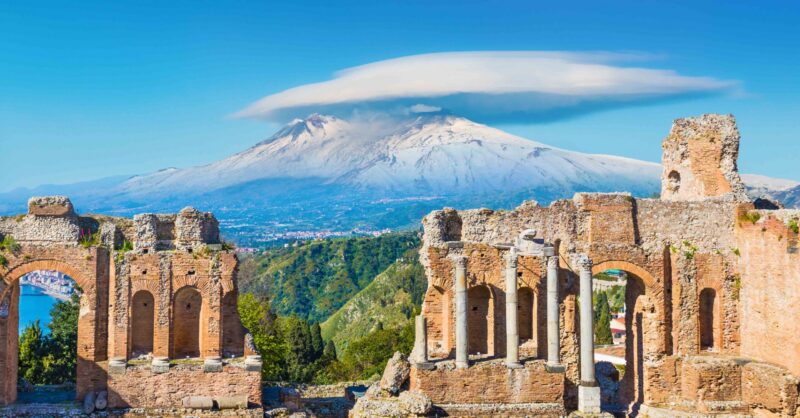 Ancient Greek theatre in Taormina on background of Etna Volcano, Italy. Taormina located in Metropolitan City of Messina, on east coast of island of Sicily.