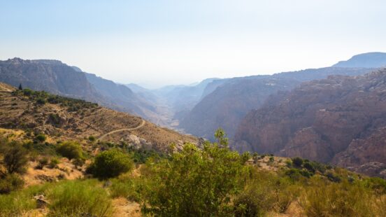 A high-angle view of a vast, rocky mountain valley under a clear blue sky in Jordan.