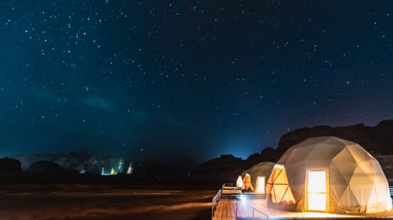 Several glowing white dome tents at night under a clear sky filled with bright stars.
