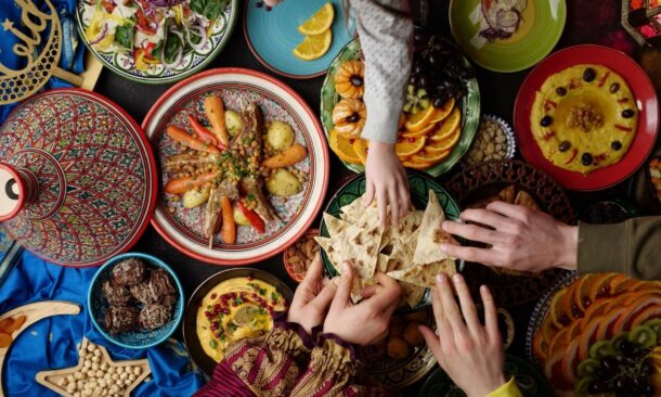 Hands reaching for flatbread on a table filled with various Middle Eastern dishes like hummus and tagine.
