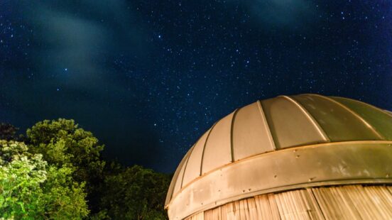Close-up of a rounded astronomical observatory dome under a clear, starry night sky with trees to the left.