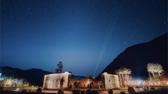 Circular resort structure with geometric patterns under a clear starry sky with a green laser pointing upwards.