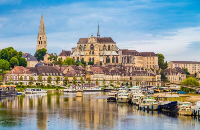 Historic town of Auxerre with Yonne river, Burgundy, France. Old buildings including a large cathedral and church spire are visible on the skyline, and there are lots of small boats moored in the harbour