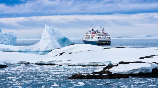 A small cruise ship by a large iceberg in Antarctica