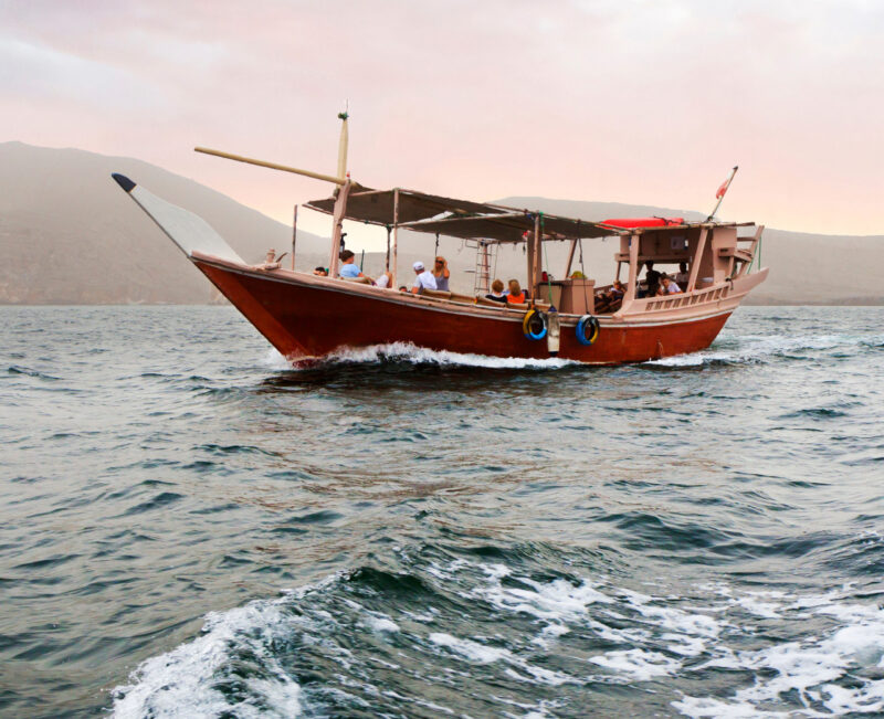 A wooden dhow boat with passengers sailing on the sea during luxury Oman trips.