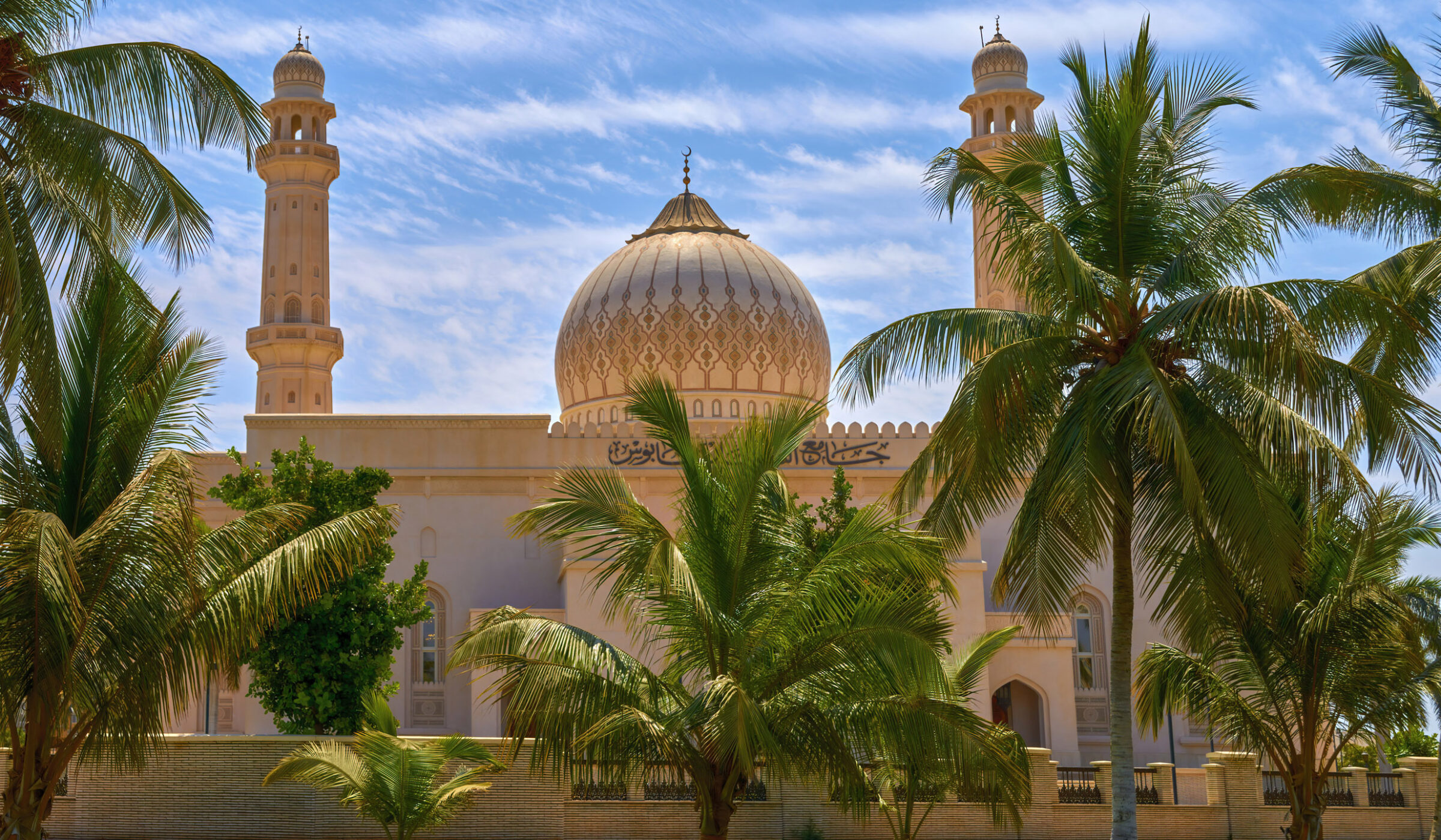 A beautiful white mosque with golden domes seen through palm fronds on luxury Oman trips.