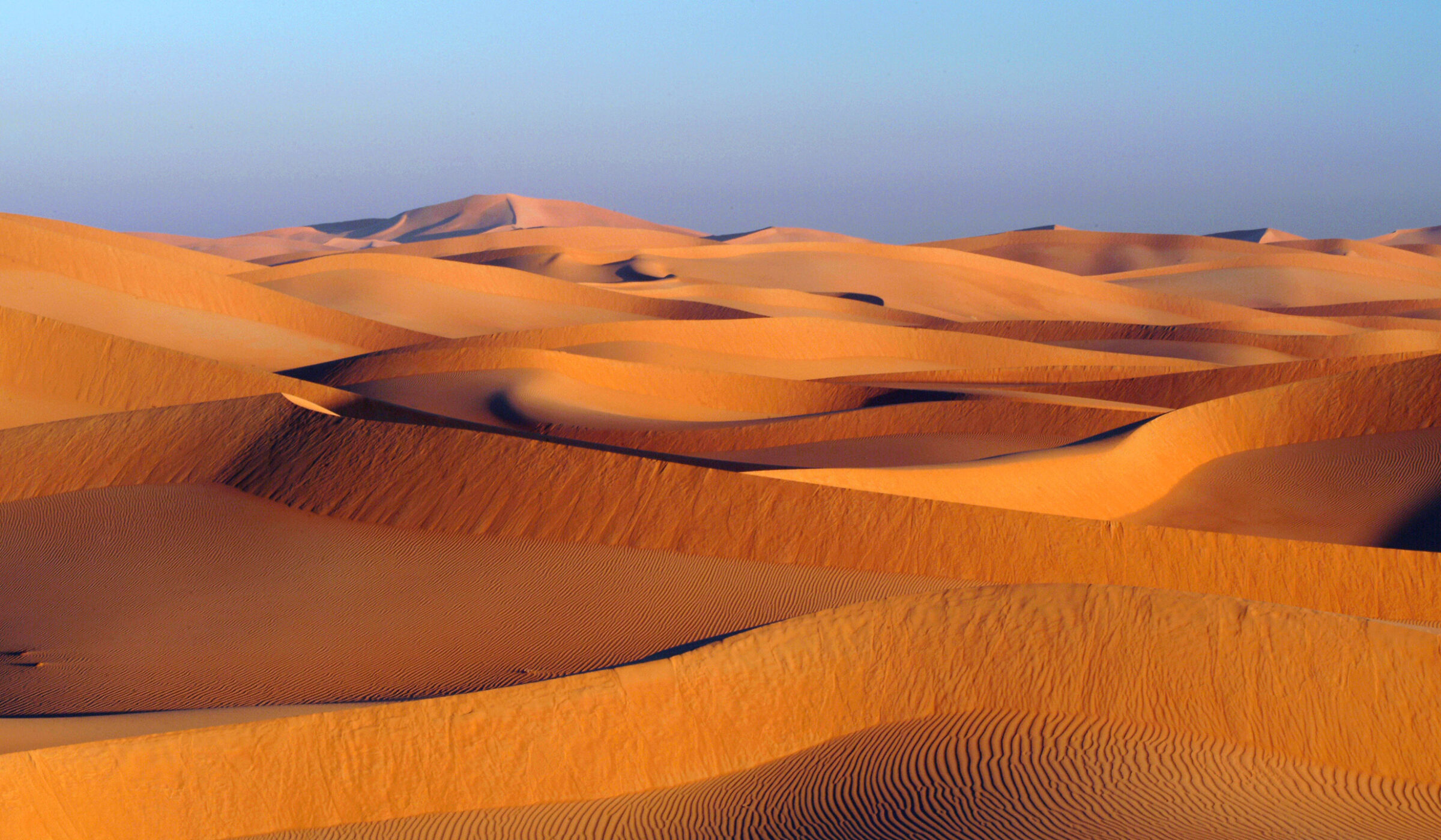 Sweeping orange sand dunes under a clear sky, typical of luxury Oman vacations.
