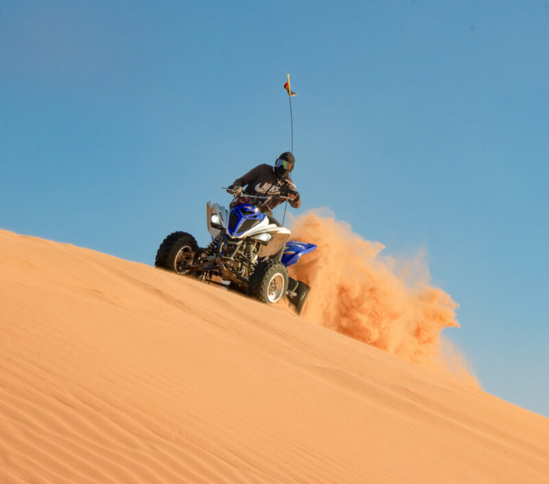 A person on a quad bike in a desert, scattering sand on a dune