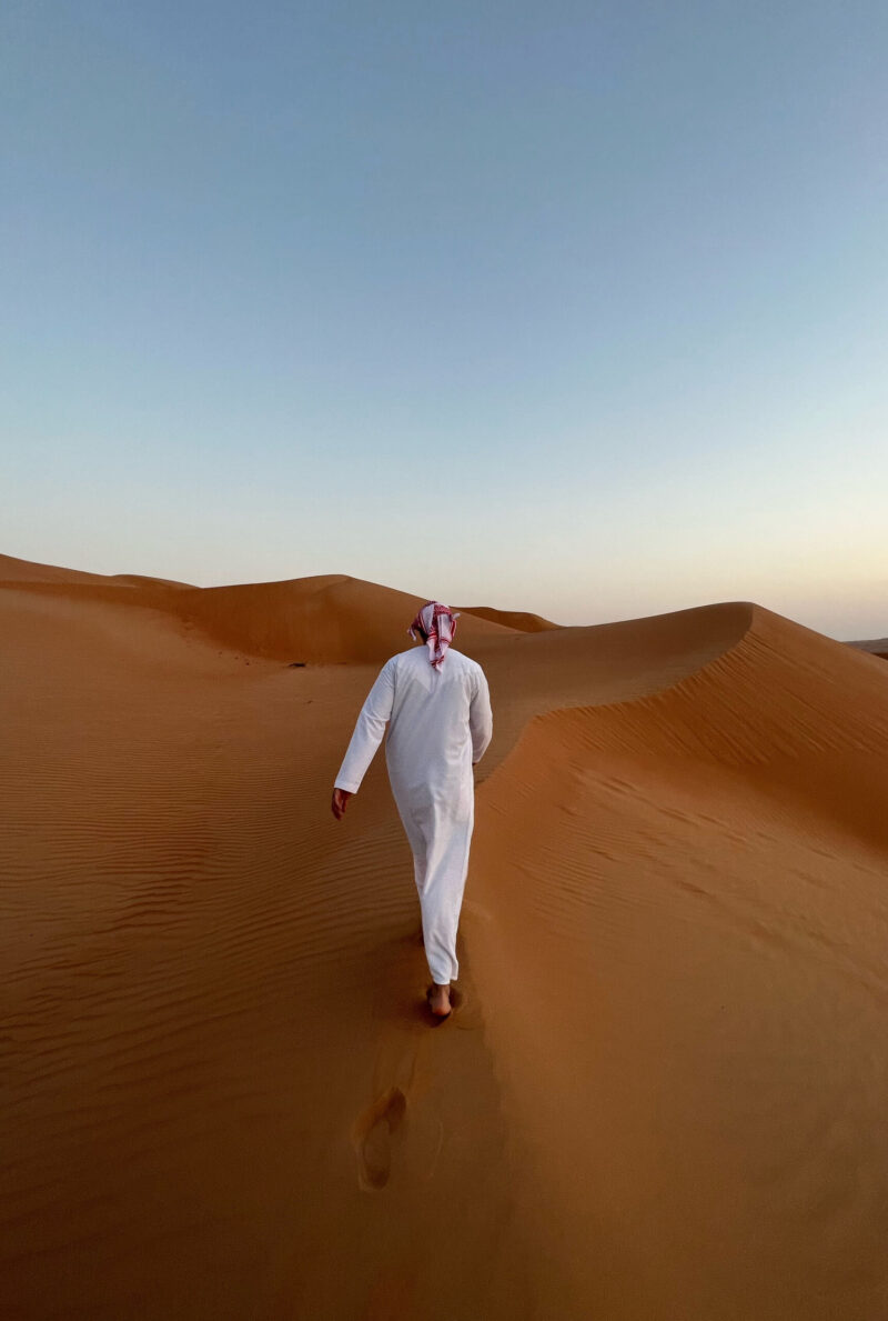 A person in a white outfit walking over a sand dune