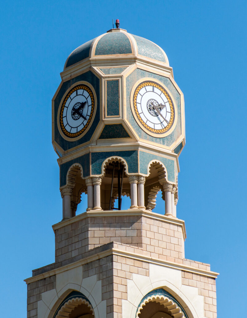 A decorative green and tan clock tower against a clear blue sky on luxury Oman holidays.