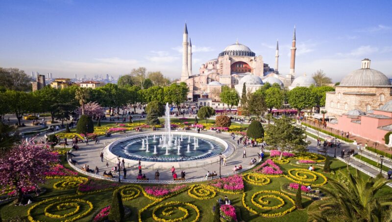 A large circular fountain and colorful flower beds in front of the Hagia Sophia during luxury Turkey Asia trips.