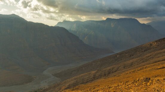 Sunlit mountain ridges and a deep valley under a dramatic cloudy sky