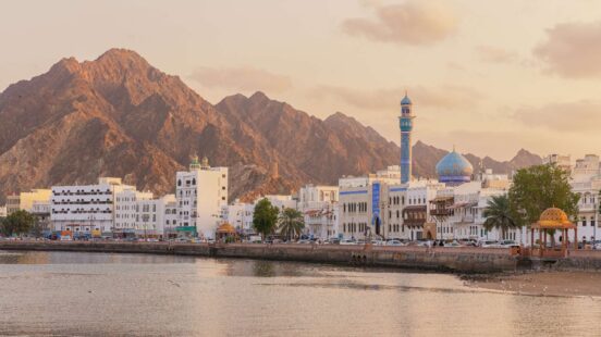 Waterfront city with a blue mosque and white architecture in front of large brown mountains.