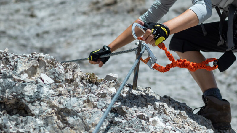 Close-up of a climber's hands using safety equipment on a fixed-rope mountain climbing route.