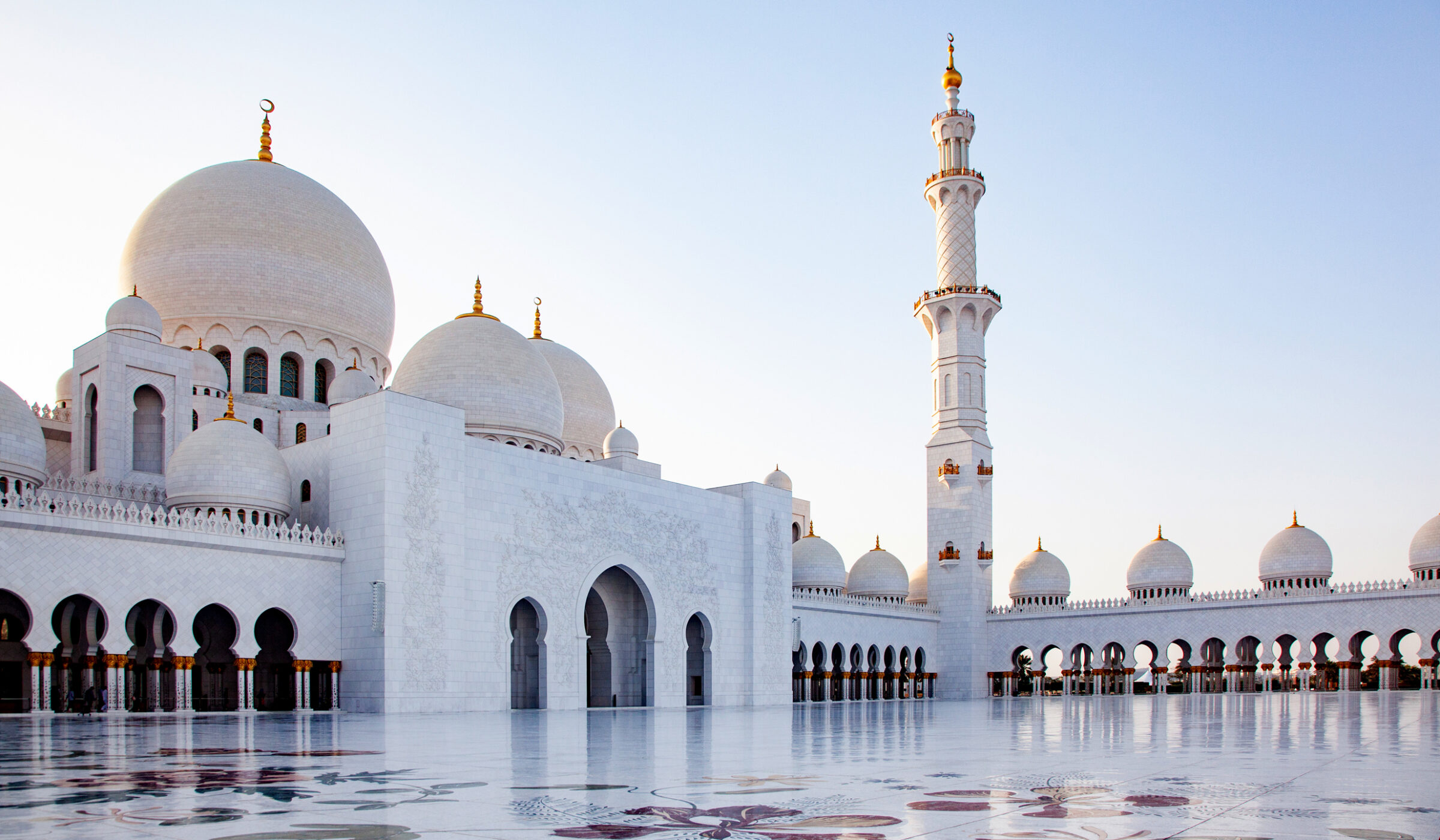 White marble courtyard and domes of the Sheikh Zayed Grand Mosque for luxury United Arab Emirates trips.