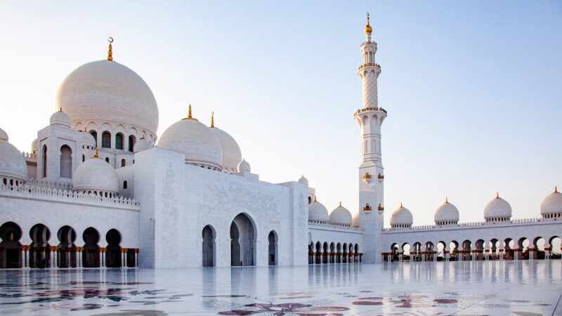 White marble courtyard and domes of the Sheikh Zayed Grand Mosque for luxury United Arab Emirates trips.