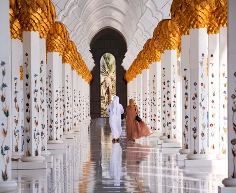 Couple walking through white marble arches with floral columns for luxury United Arab Emirates holidays.