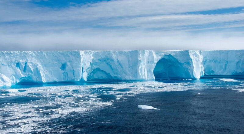 Blue iceberg with caves and ice floe in Admiralty Bay, Antarctica.