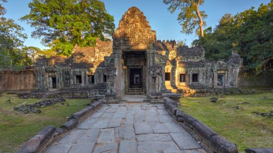A stone pathway leading to the ancient carved entrance of a weathered Khmer temple at sunset.