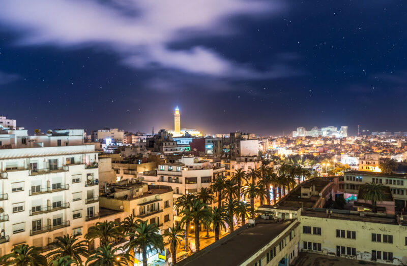 Cityscape from Casablanca- Iluminated Avenue with palms leading to the famous landmark Hassan Mosque II. Casablanca at night.
