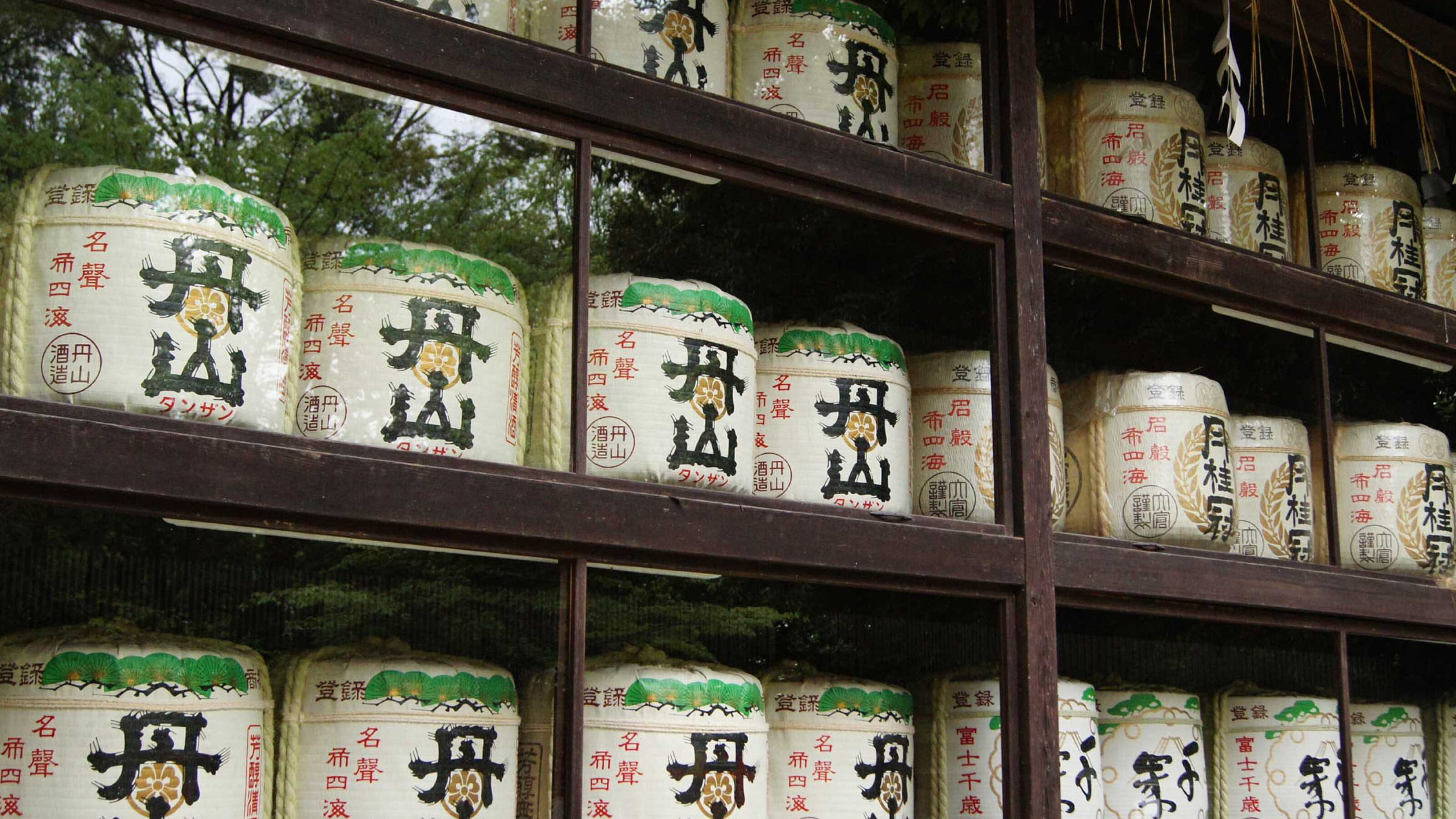 Rows of white sake barrels decorated with black Japanese characters and green accents stacked on shelves.