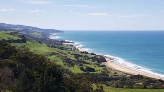 Rolling green hills overlooking a long coastline with blue ocean waves and a distant sandy beach.